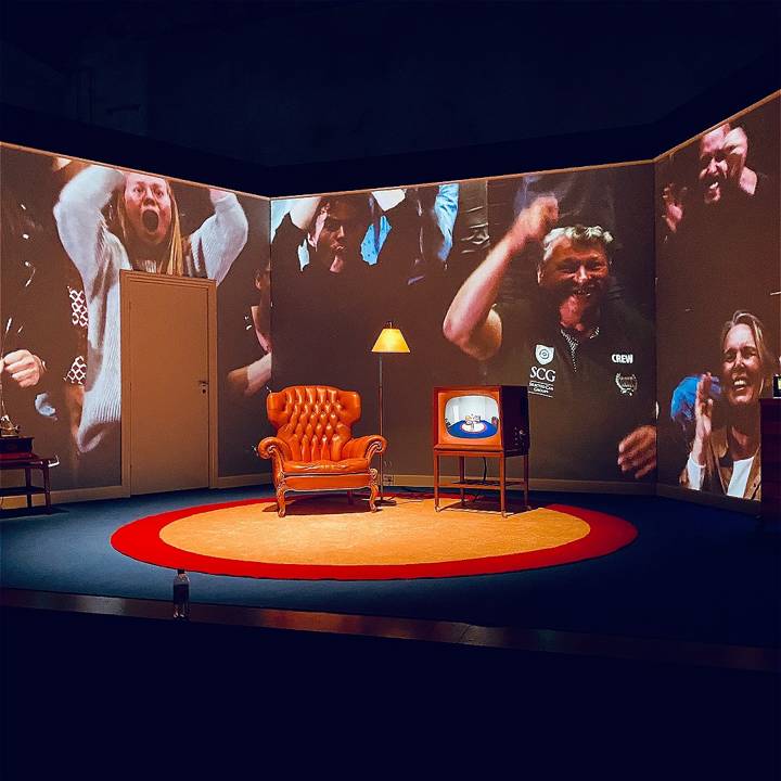 Set image from the show Champions showing an old wingback armchair, an old style television and a backdrop of images of a football crowd